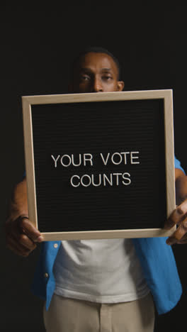 Vertical-Video-Portrait-Of-Vertical-Video-Shot-Of-Man-Holding-Your-Vote-Counts-Sign-In-Election-Against-Black-Background